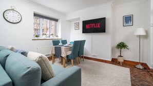 Un salon moderne comprenant un canapé, une table à manger, des chaises, un téléviseur, une horloge et une plante en pot.