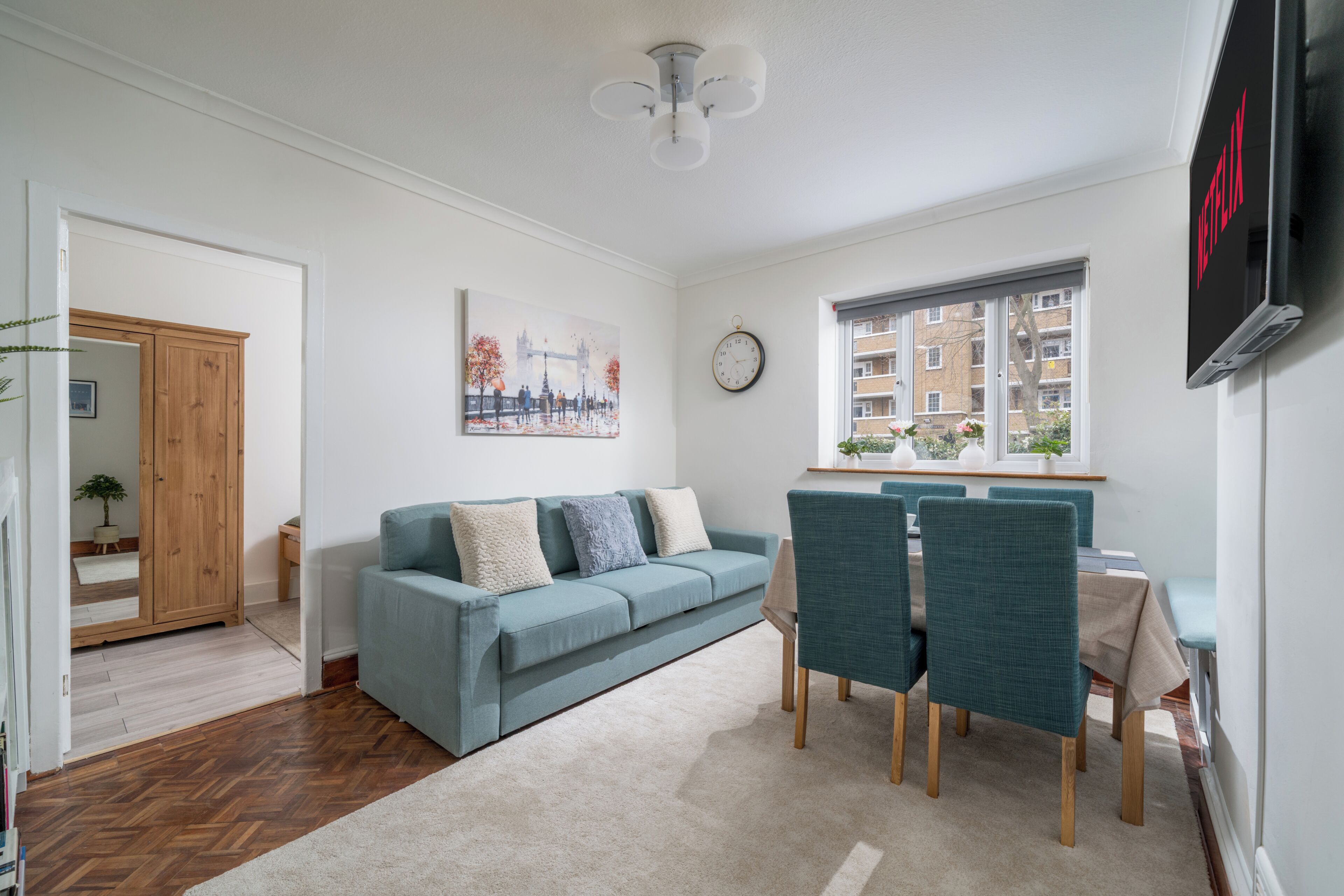 Un salon moderne comprenant un canapé, des fauteuils, une table à manger, une horloge et une fenêtre donnant sur des immeubles.