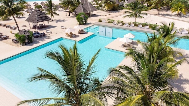 Un resort con piscina, playa y edificios de techo de paja.