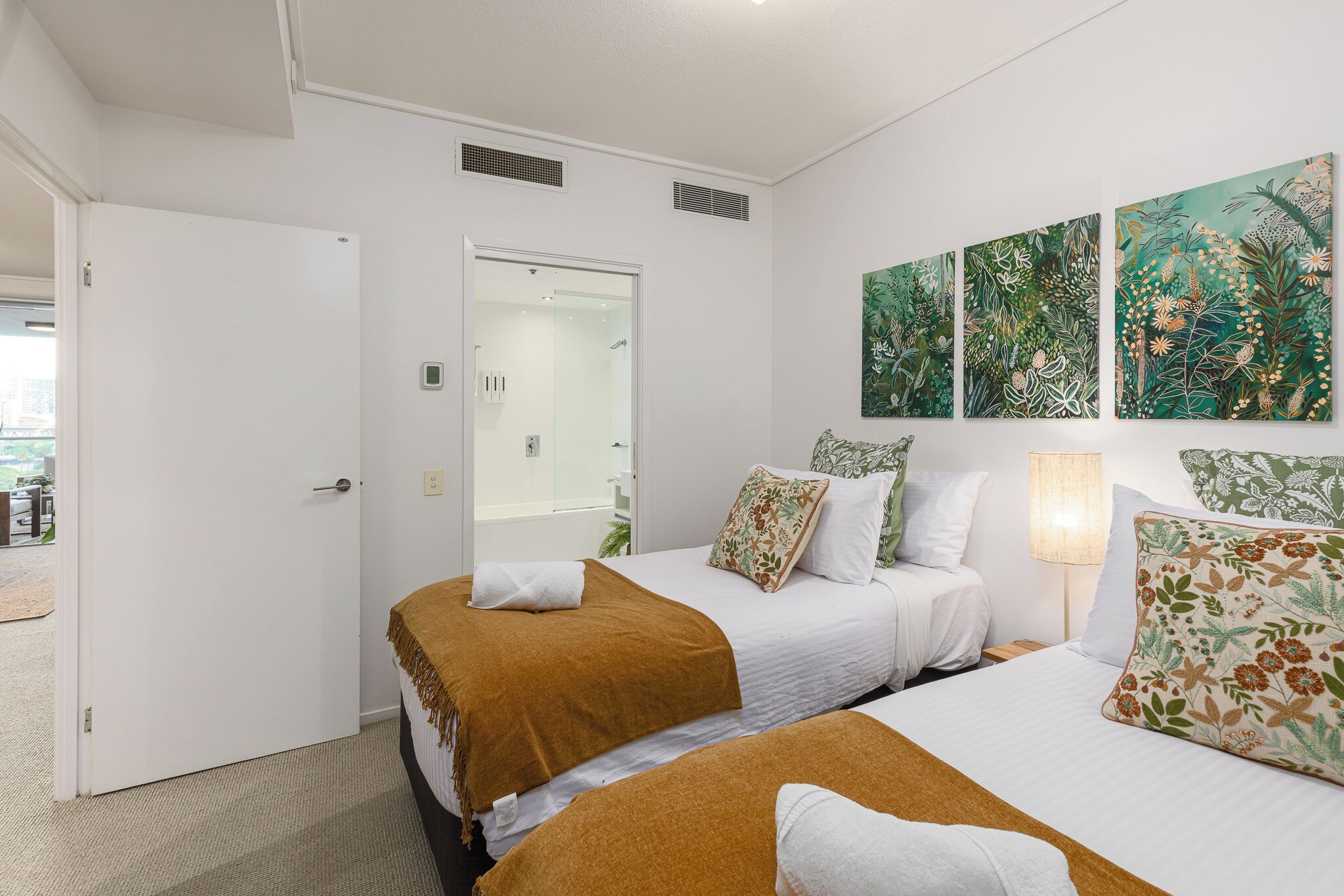 A hotel room with two beds, a shower, and three wall-mounted artworks.