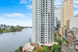 A high-rise building with a curved facade, a river in the background, and a Marriott hotel adjacent to it. - Tropical City Escape (Brisbane)