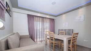 A modern living room with a sofa, dining table, chairs, and a large window with curtains.