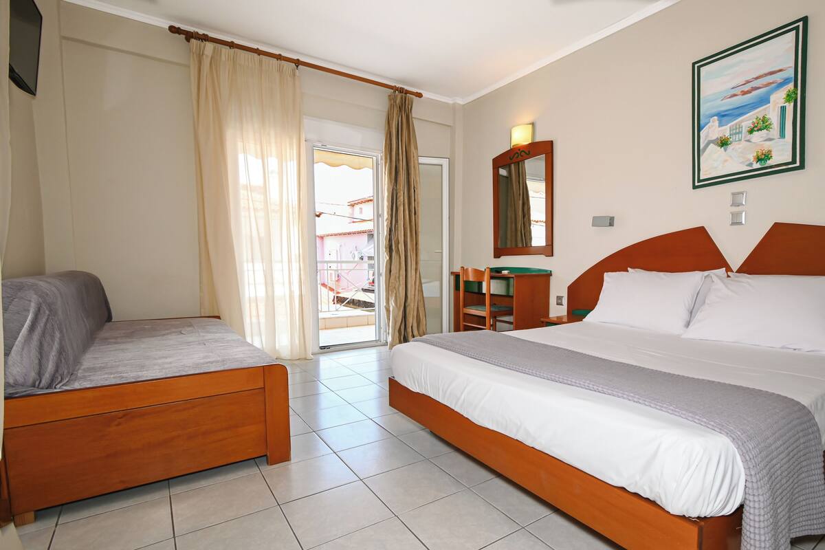 Una habitación de hotel con cama, sofá, escritorio y ventana con cortinas.