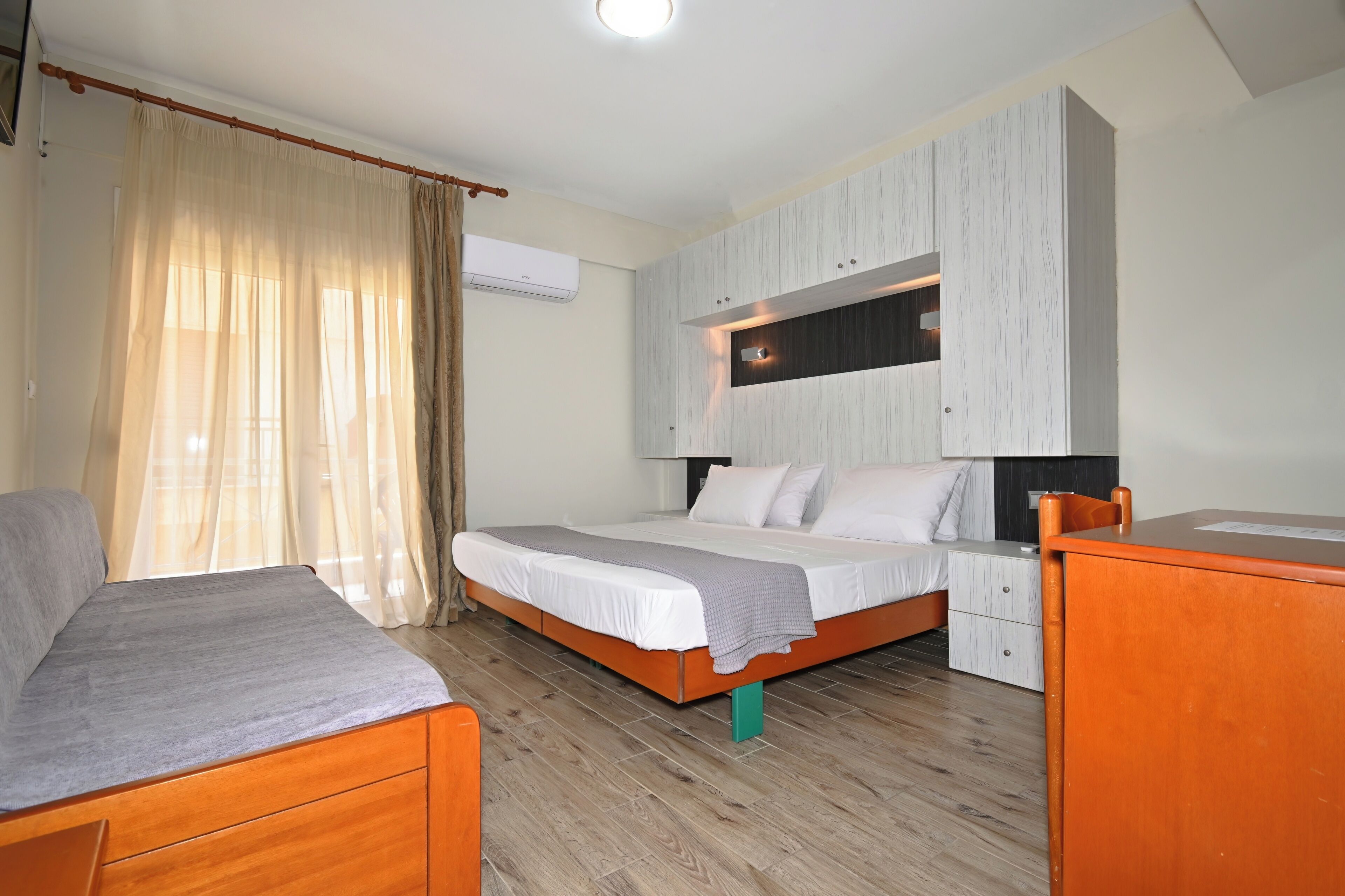 A bedroom with a bed, a desk, a chair, a wardrobe, and an air conditioning unit.