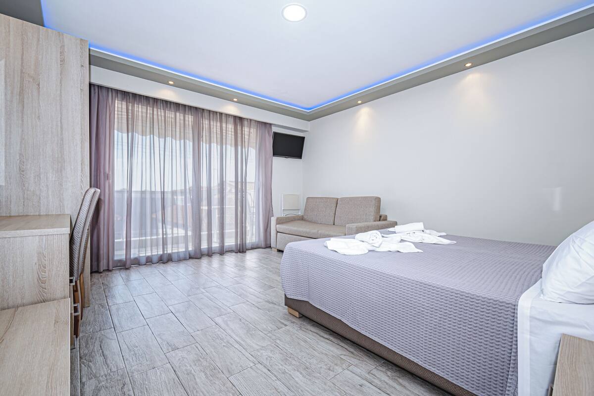 Una habitación de hotel moderna con una cama, un sofá, un escritorio y un televisor.
