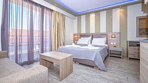 A hotel room with a bed, bedside tables, a desk, a chair, and a view through large windows.