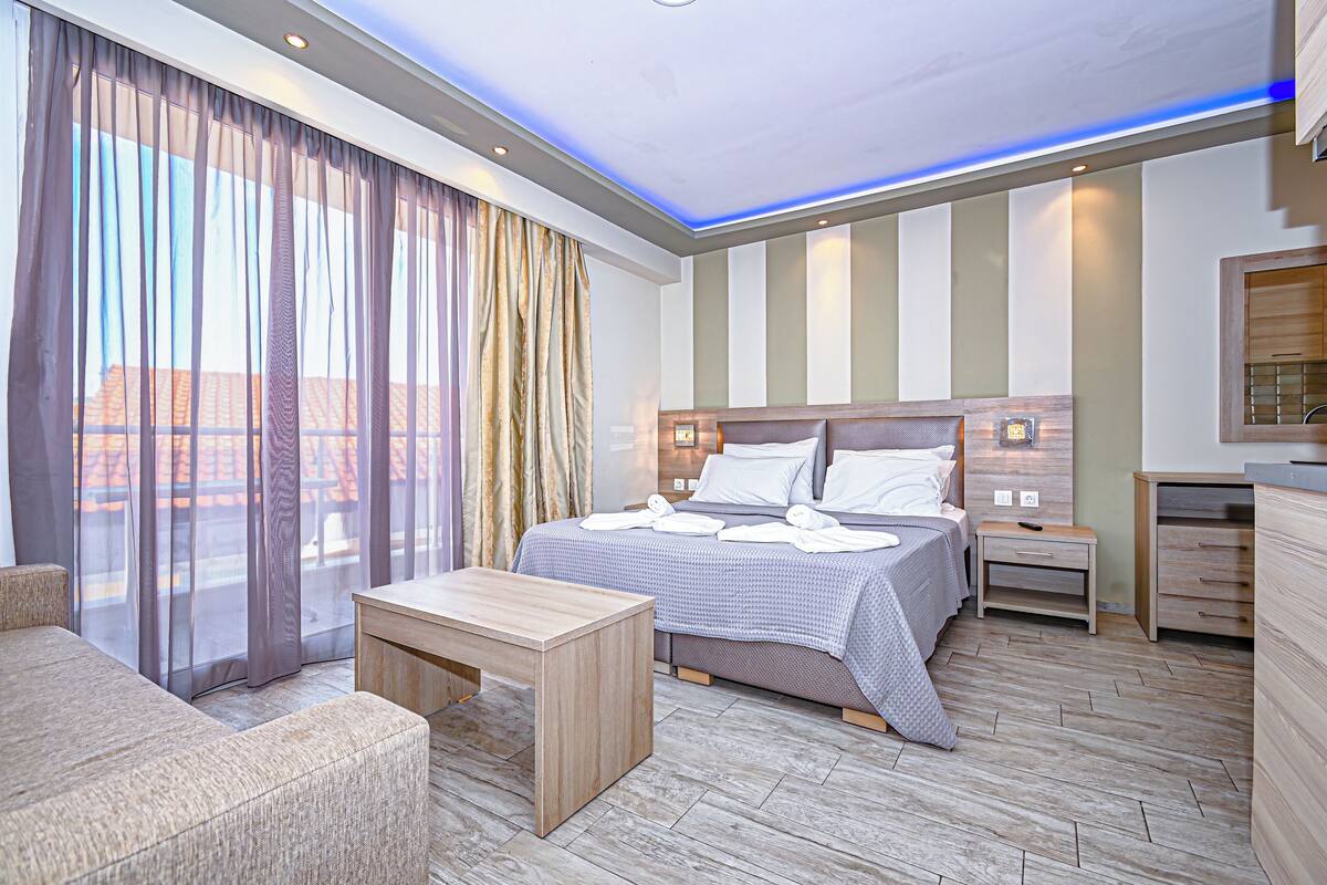 Habitación de hotel con cama, mesitas de noche, escritorio, silla y vistas amplias a través de grandes ventanales.