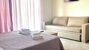 A hotel room with a bed, a sofa, an air conditioning unit, and a television.
