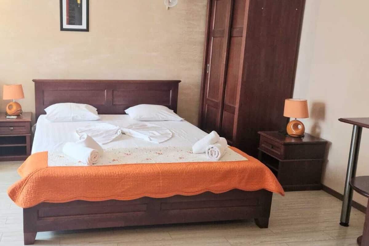 A hotel room with a bed, a sofa, two bedside tables with lamps, and a wooden wardrobe.