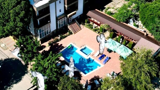 A multi-story building with a rooftop pool, surrounded by lush greenery and a view of the sea. - Naparis Boutique  (Eforie Sud)
