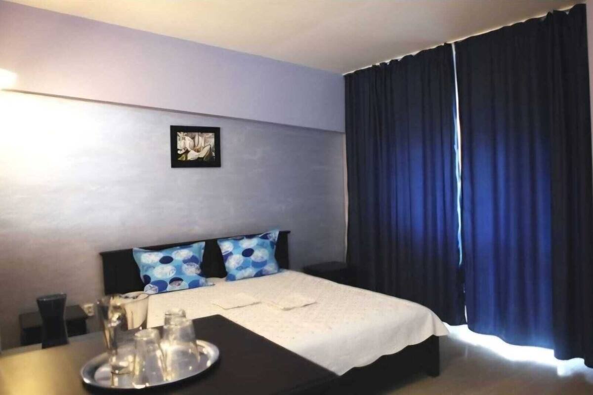 A hotel room with a bed, a bedside table with a tray, a picture on the wall, and a window with dark curtains.