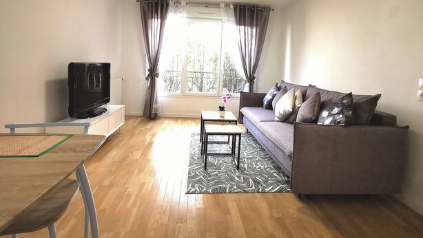 A living room with a sofa, a television, a small table, and a window with curtains. - Créteil, comfortable apartment 700m from the metro. Private parking lot (Créteil)