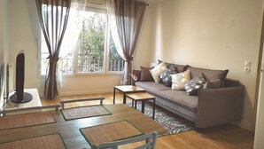 A living room with a sofa, a TV, a dining table with placemats, and a window with curtains. - Créteil, comfortable apartment 700m from the metro. Private parking lot (Créteil)