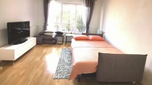 A bedroom with a bed, a TV, a small table, a window with curtains, and a view of trees. - Créteil, comfortable apartment 700m from the metro. Private parking lot (Créteil)