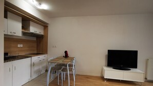 A modern kitchen with white cabinets, a wooden countertop, and a dining area with a table and chairs. A flat-screen TV is mounted on a white cabinet. - Créteil, comfortable apartment 700m from the metro. Private parking lot (Créteil)