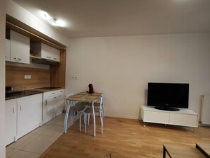 Eine moderne Küche mit weißen Schränken, einer Holz Arbeitsplatte und einem Essbereich mit Tisch und Stühlen. Ein Flachbildfernseher ist an einem weißen Schrank befestigt.
