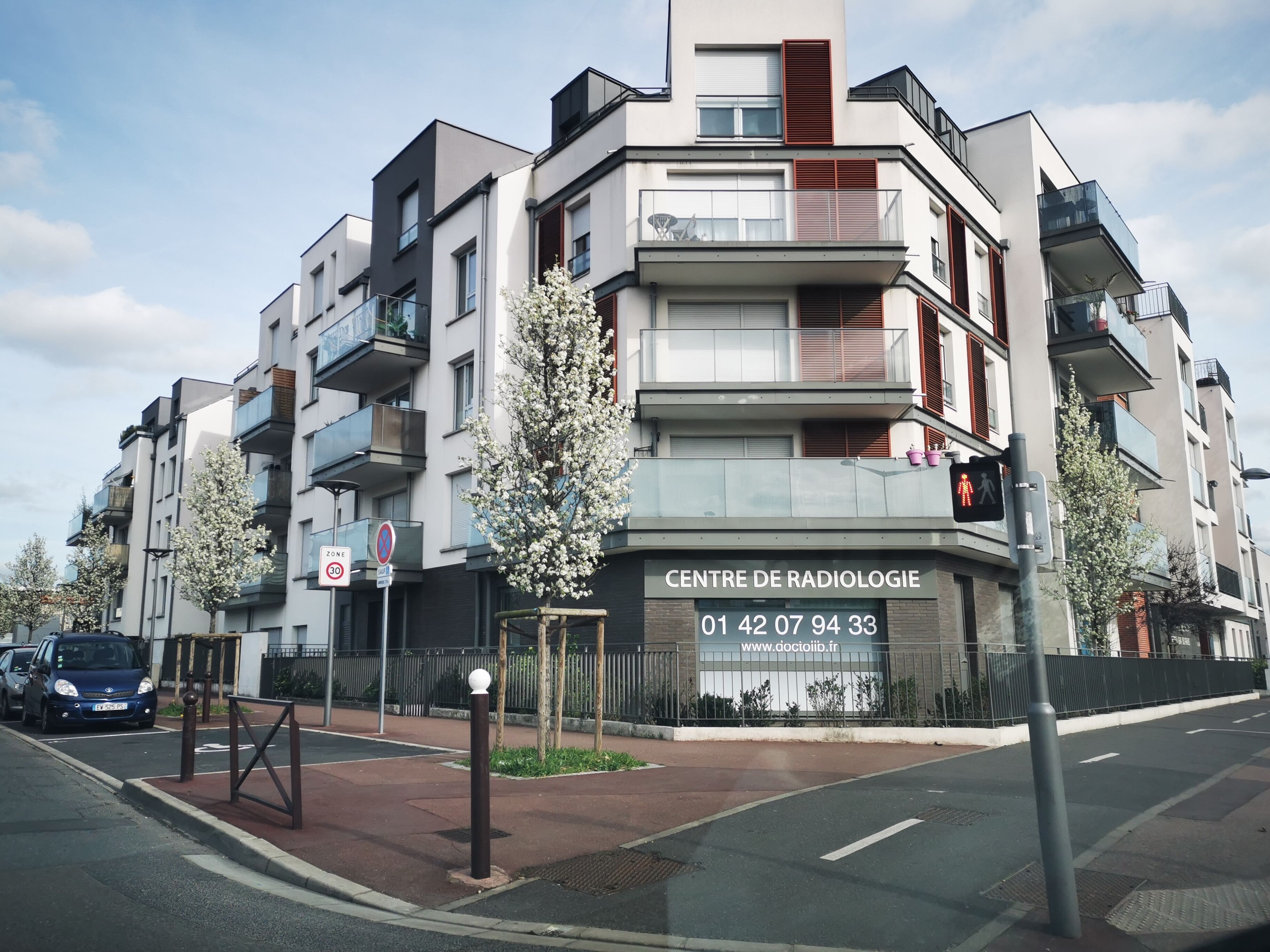 Un edificio de varios pisos con balcones, un cartel que dice 'CENTRE DE RADIOLOGIE' y un número de contacto.