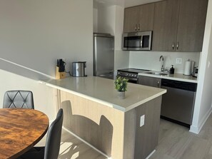 Een moderne keuken met een centraal eiland, roestvrijstalen apparatuur en een eetgedeelte met een houten tafel en stoelen.