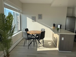 Een moderne keuken met een centraal eiland, een zithoek met een ronde tafel en stoelen, en een groot raam met zonwering.