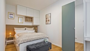 A bedroom with a bed, bedside table, bench, wardrobe, and wall-mounted cabinets. - Gleam Homes Dresden HafenCity Urban District (Dresden)