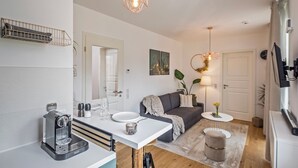 A modern kitchen with a coffee machine, a dining table, and a sofa in a living area. - Gleam Homes Dresden HafenCity Urban District (Dresden)