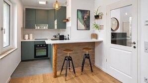 A modern kitchen with a central island, bar stools, a hanging light fixture, and a large window. - Gleam Homes Dresden HafenCity Urban District (Dresden)