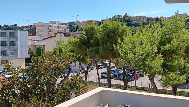 Un balcó amb vista a un pàrquing, edificis i arbres.