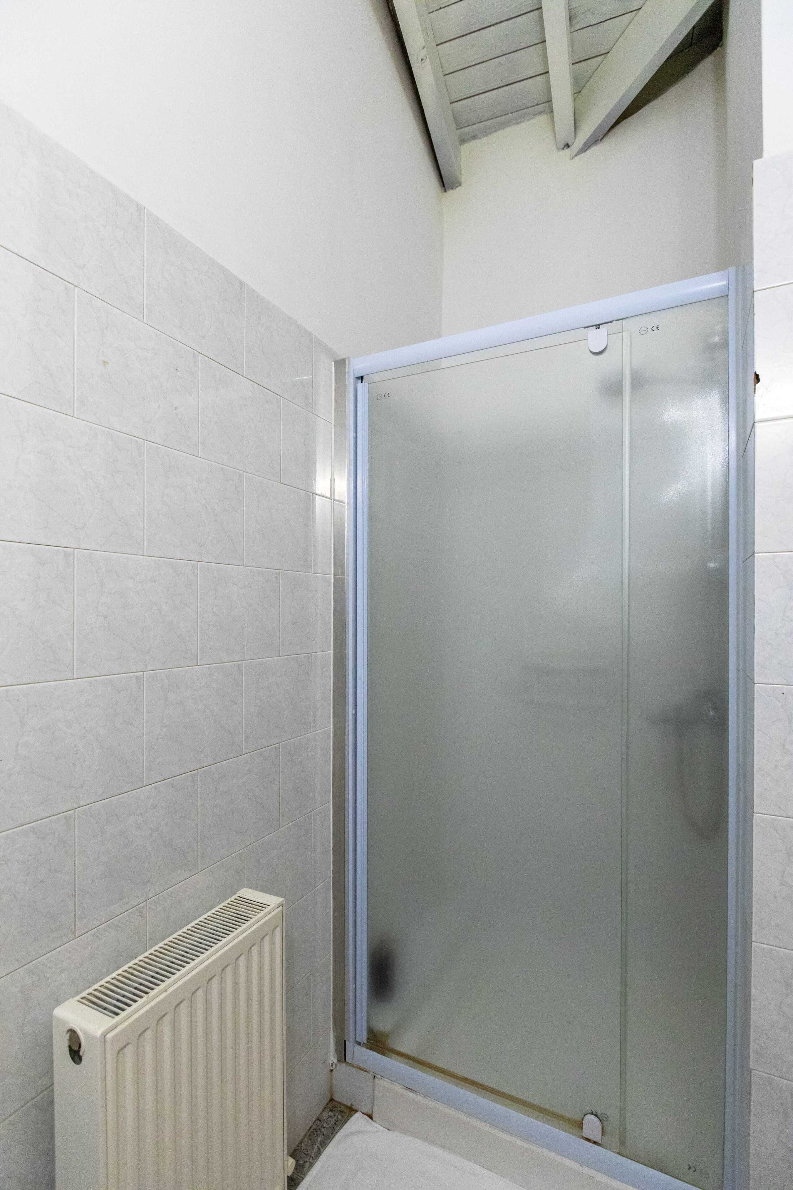 A bathroom with a glass shower enclosure, white tiled walls, and a white radiator.