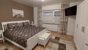 Una camera da letto con un letto, comodini, un termosifone, una finestra con tende e una TV montata a parete.