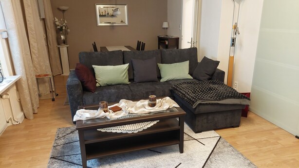 Un soggiorno con un divano grigio scuro, un tavolino in vetro e una coperta decorata.