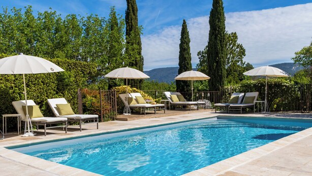 Une piscine entourée de verdure et de montagnes, avec des chaises longues et des parasols.