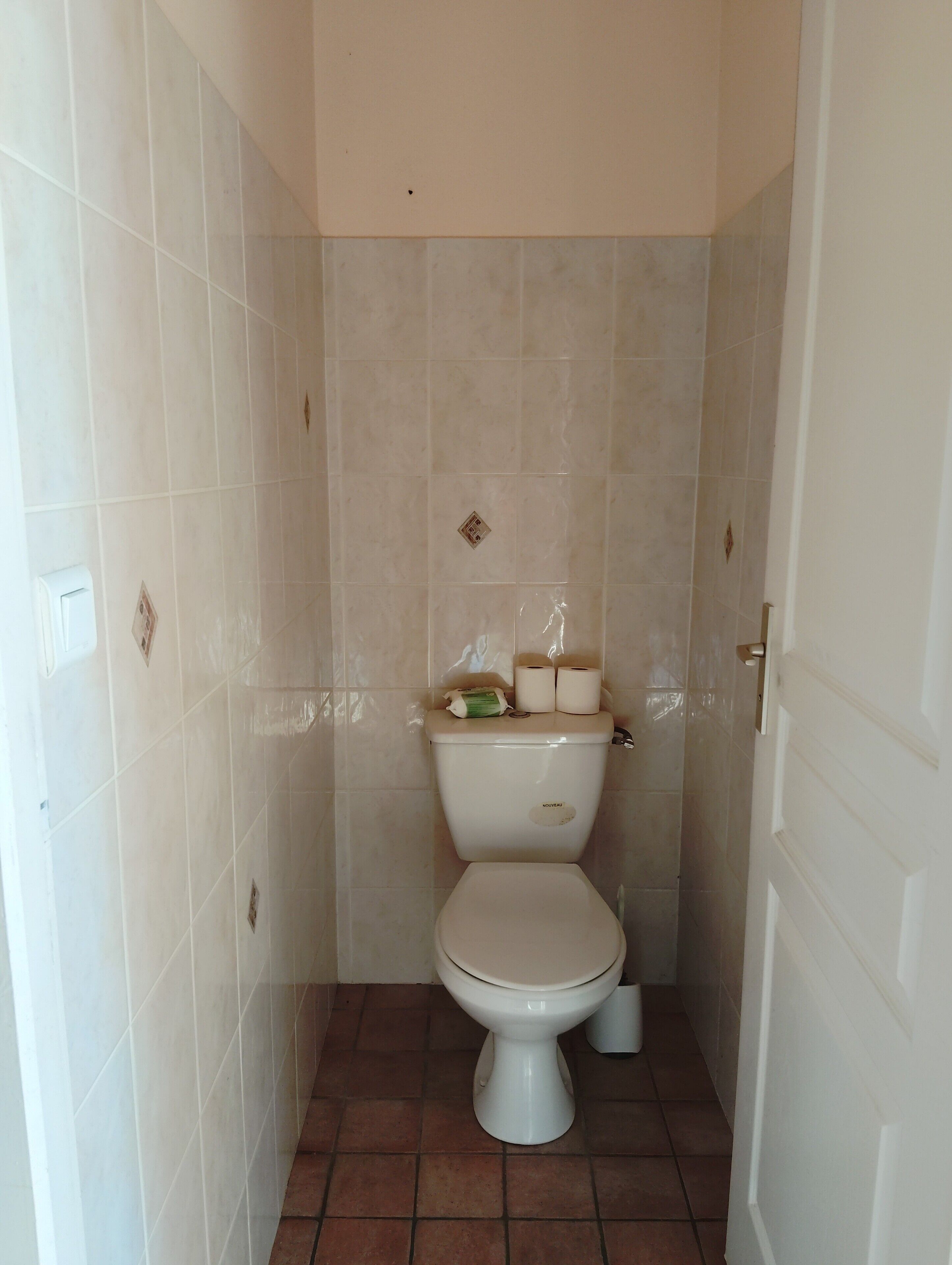 Une petite salle de bain carrelée, avec des toilettes, une porte blanche et un sol carrelé.