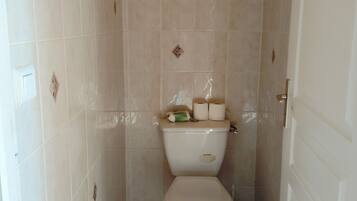 Une petite salle de bain carrelée, avec des toilettes, une porte blanche et un sol carrelé.