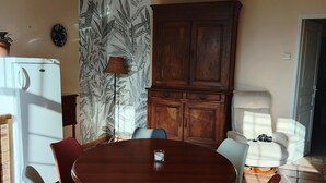 Un coin repas comprenant une table ronde en bois, six chaises, un réfrigérateur blanc, un meuble en bois et un mur décoré d’un motif.