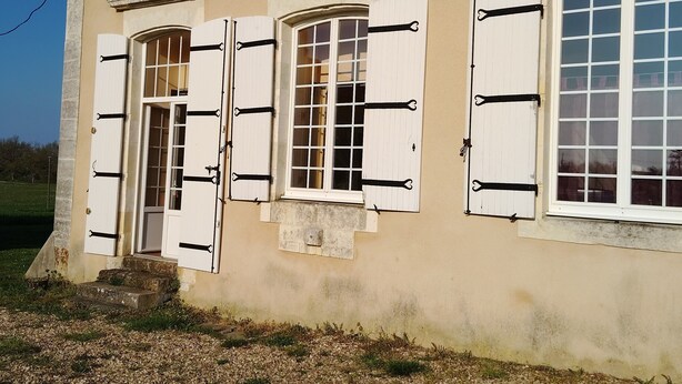 Un bâtiment à la façade beige, doté de nombreuses fenêtres avec volets et d’une petite entrée avec des marches.