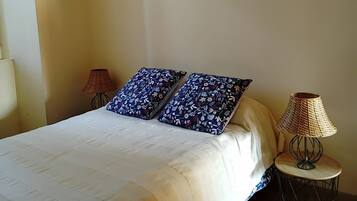 Een slaapkamer met een bed, twee kussens, een schilderij, een lamp en een klein tafeltje.