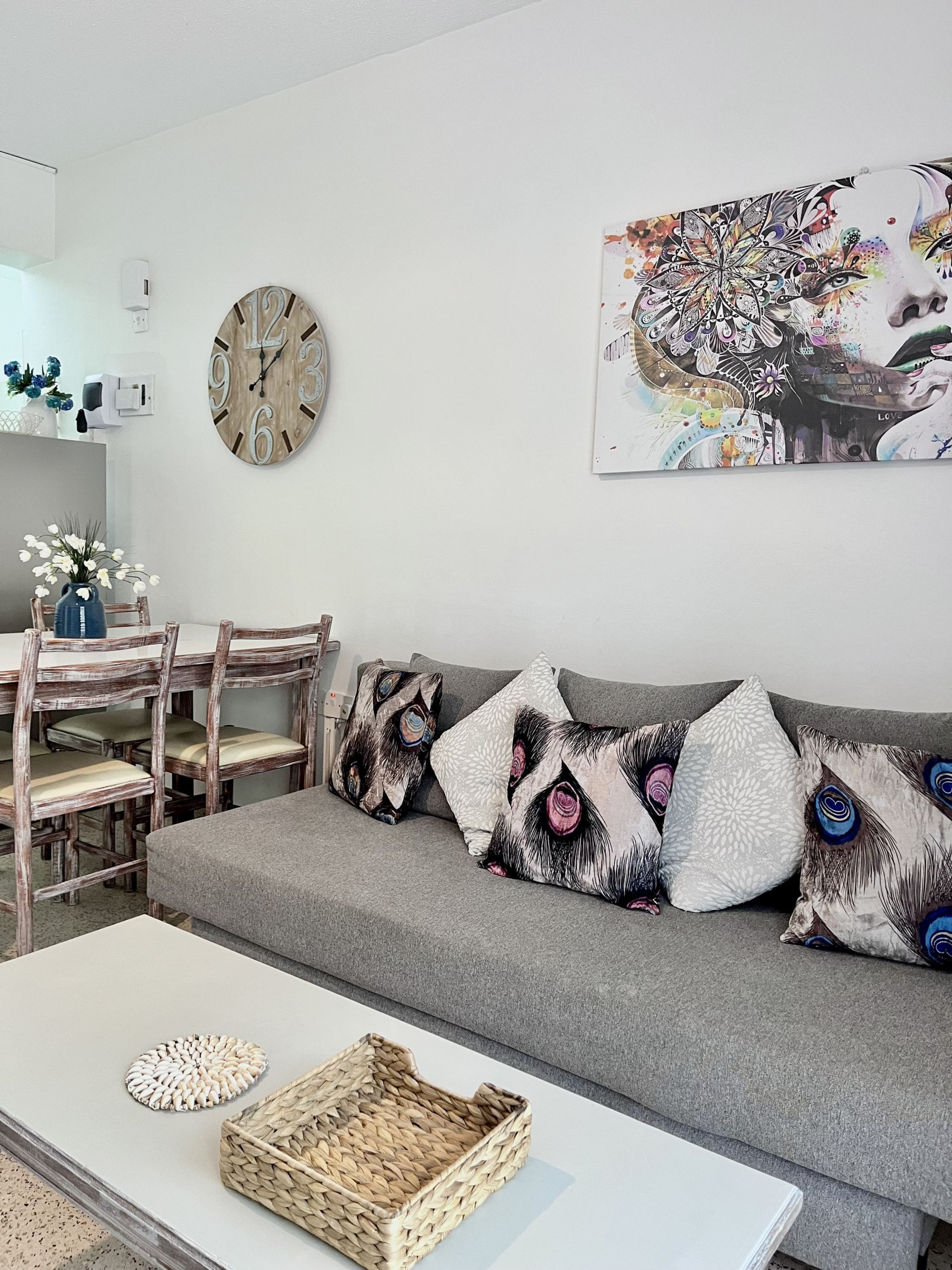 Una sala de estar con un sofá gris, una mesita de centro blanca y un reloj de pared.