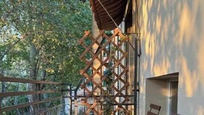 Ein Balkon mit Holztisch und -stühlen, einem Metallzaun und Blick auf Bäume.