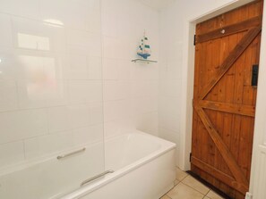 A bathroom with white tiles, a white bathtub, a wooden door, and a small shelf with a model sailboat. - NO 10 (Portland)