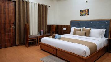 A hotel room with a wooden bed, a desk with a chair, a grey rug, and a painting on the wall.