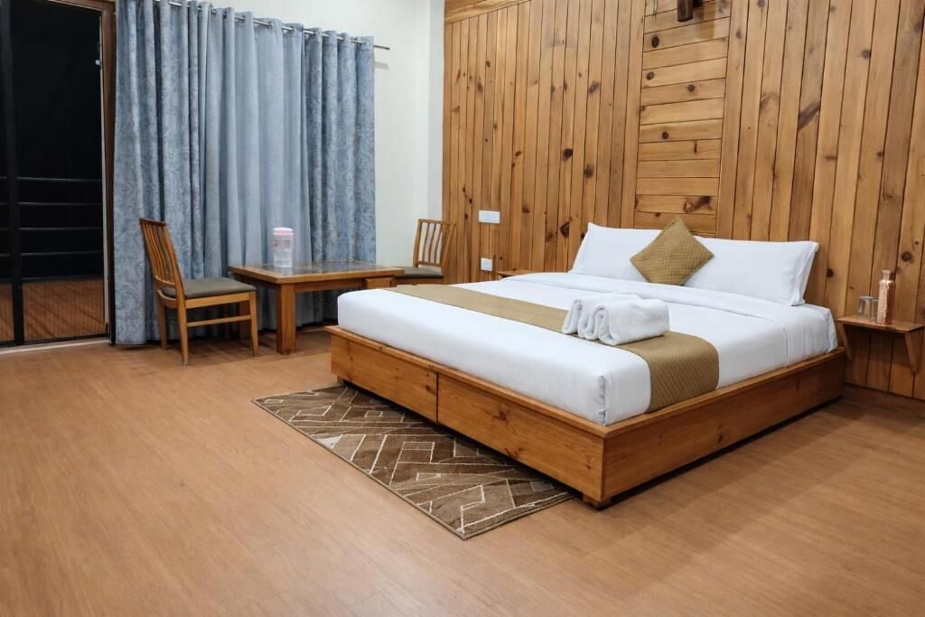 A bedroom with a wooden bed, a desk, chairs, and a view through a curtain.
