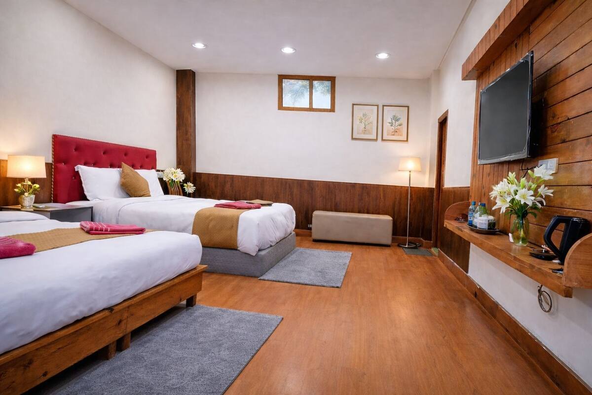 A hotel room with two beds, a wooden headboard, a TV, a desk, and a bench.