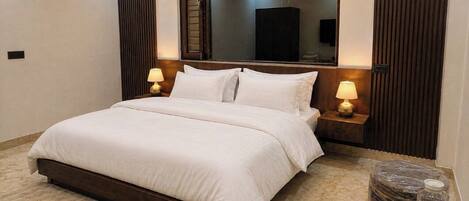 A hotel room with a large bed, two bedside tables with lamps, a mirror above the bed, and a ceiling fan.