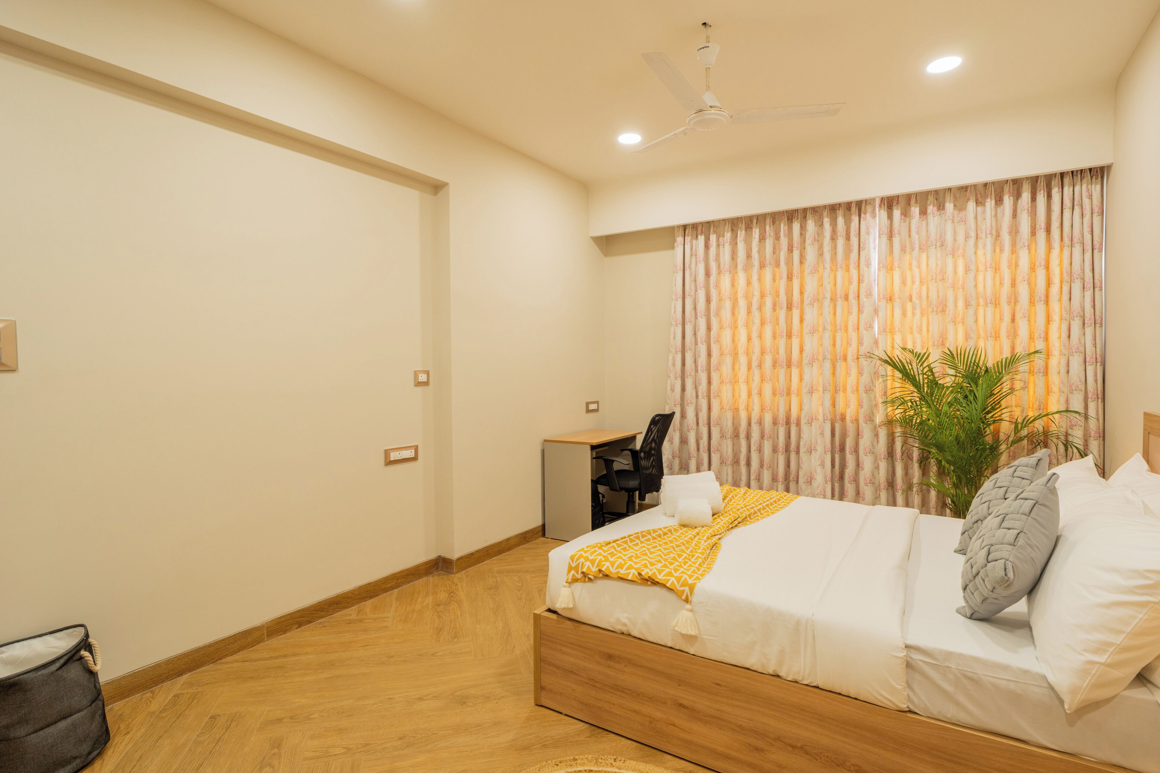 A bedroom with a bed, a desk, a chair, a ceiling fan, and a window with curtains.
