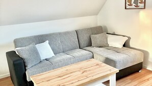 A modern living room with a grey sectional sofa, a wooden coffee table, and a framed artwork of sailboats on the wall. - Cozy vacation apartment Vechteglück (Emlichheim)