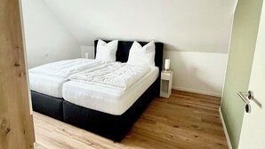 A bedroom with a bed, a bedside table, a nightstand, and a wooden floor. - Cozy vacation apartment Vechteglück (Emlichheim)