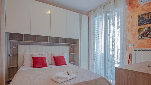 Ein Schlafzimmer mit einem großen Bett, weißen und roten Kissen, einem weißen Kopfteil und einem Holzschrank.