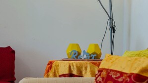 Ein Zimmer mit einem Tisch, der mit einer gelben Tischdecke bedeckt ist, einem roten Stuhl und einem weißen Sofa.
