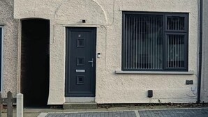 A building with a dark door, a window with vertical bars, and a textured facade. - Dale Combe, 3 Bedroom House 5 Star on air bnb (Manchester)