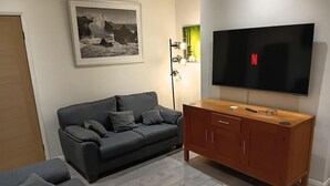 A living room with a grey sofa, a wooden cabinet, a flat-screen TV, and a framed picture on the wall. - Dale Combe, 3 Bedroom House 5 Star on air bnb (Manchester)